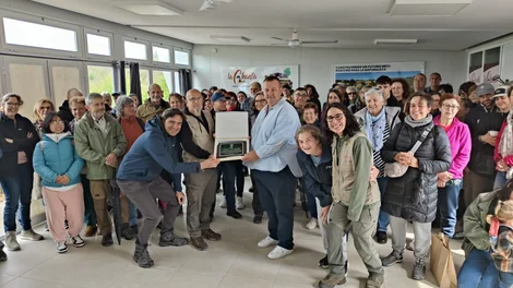 Foto grupal de los asistentes y técnicos en el interior del centro de interpretación sosteniendo una placa conmemorativa durante la jornada de puertas abiertas por el quinto aniversario del acuerdo de custodia.