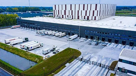 Nave industrial logística con pavimento continuo de hormigón de gran extensión, zona de carga y descarga con varios camiones estacionados y amplias superficies preparadas para tráfico pesado y operaciones industriales.
