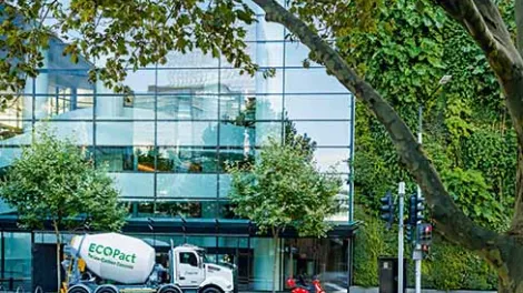 Camión hormigonera EcoPact suministrando hormigón de bajas emisiones frente a edificio urbano sostenible, ejemplo de construcción eficiente y descarbonizada.