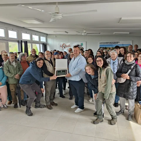 Foto grupal de los asistentes y técnicos en el interior del centro de interpretación sosteniendo una placa conmemorativa durante la jornada de puertas abiertas por el quinto aniversario del acuerdo de custodia.