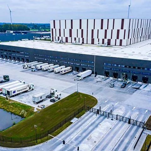 Nave industrial logística con pavimento continuo de hormigón de gran extensión, zona de carga y descarga con varios camiones estacionados y amplias superficies preparadas para tráfico pesado y operaciones industriales.